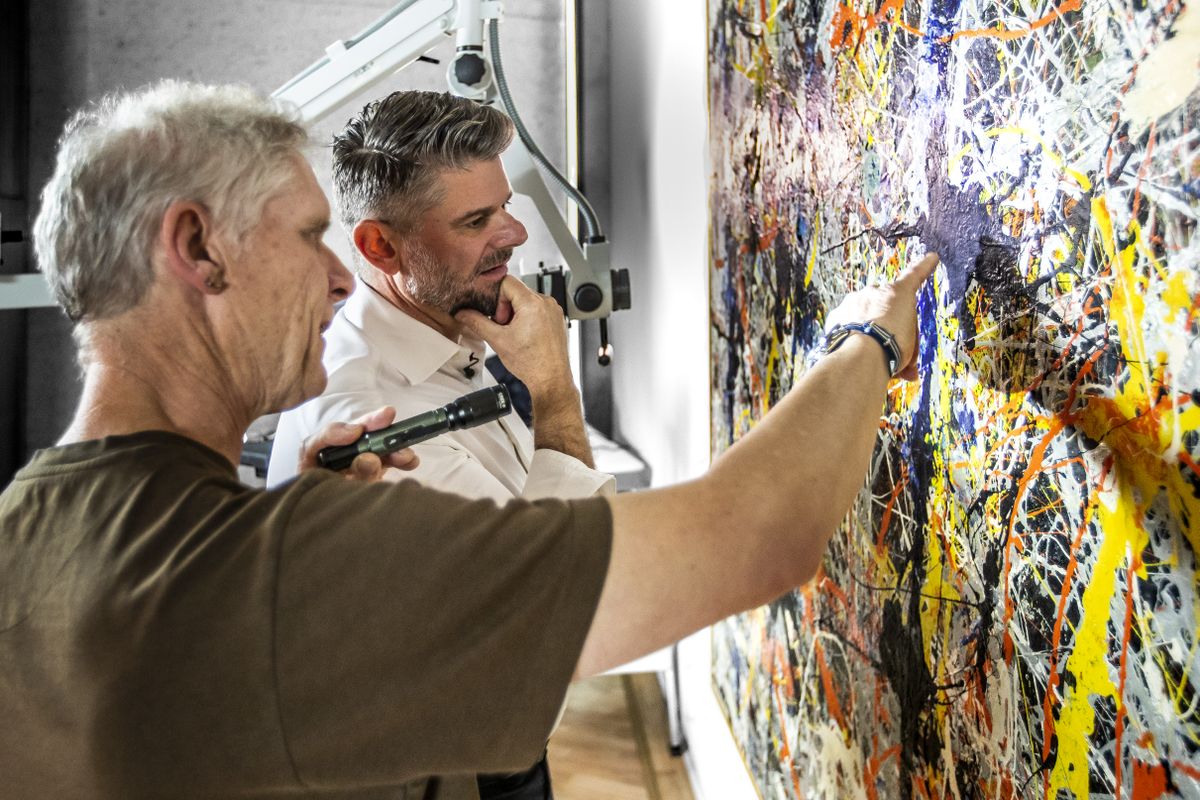 Photograph of conservator and director gesturing to painting under restoration