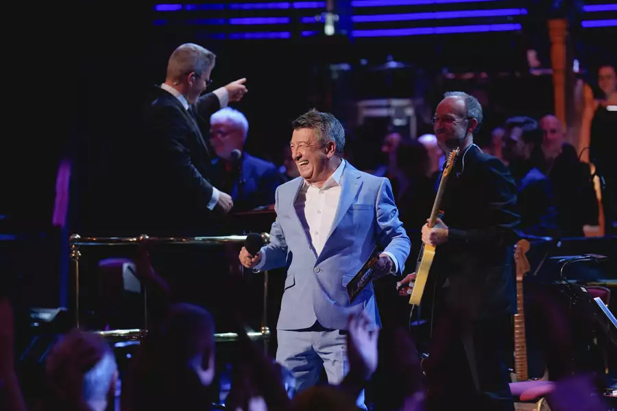 A singer performing in a grey suit with a full orchestra at the BBC Proms