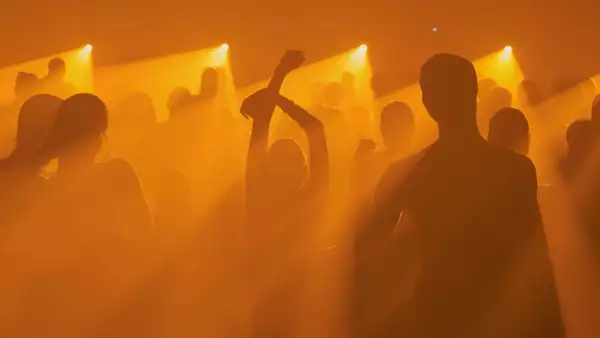 A crowd silhouetted dancing at an event bathed in orange light