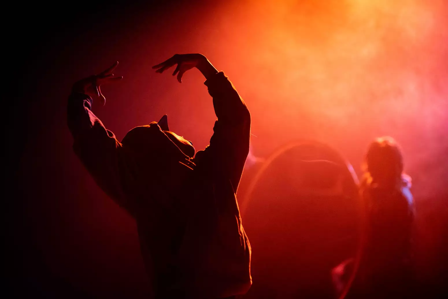A dancer on stage performing with their back turned during Traplord. The lighting is red and orange.