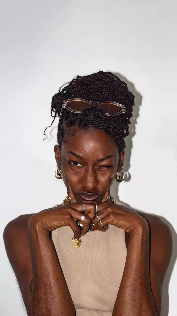 Meme Gold looks at the camera wearing rings and a light tank top