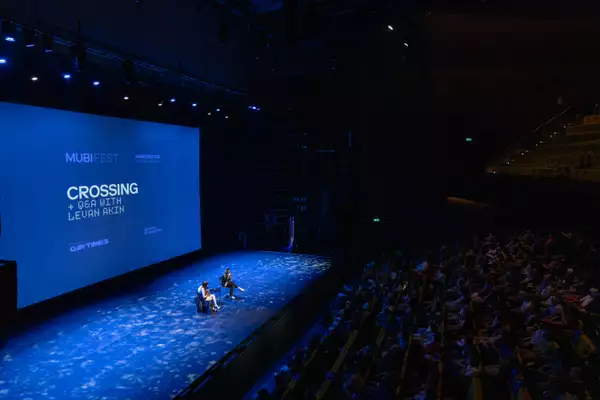 Film showing of 'Crossing' in the Hall. Two people are sat on stage for the Q&A in front of the big screen. The lighting is blue.