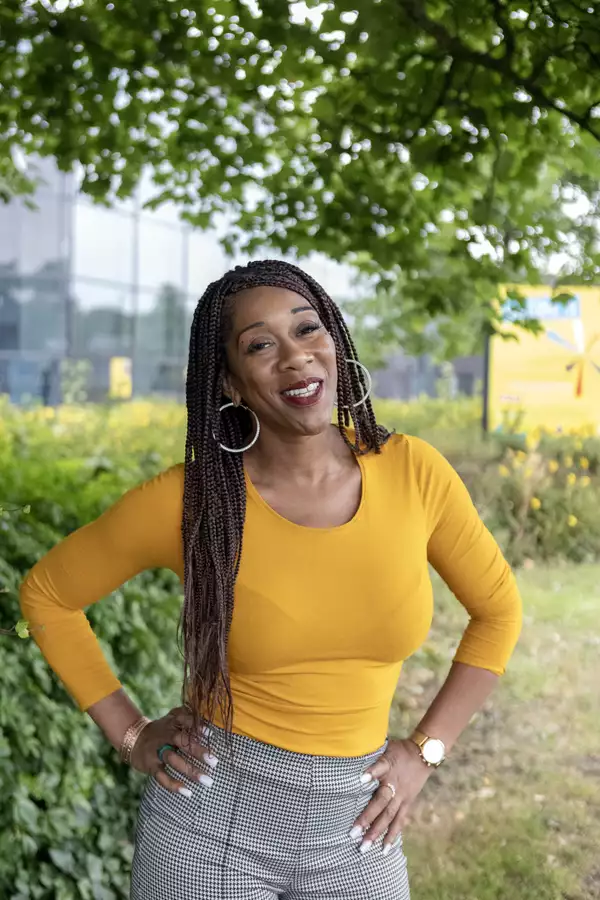 Headshot of Sharlene Small smiling and wearing a bright orange/yellow top. They are stood outside under a tree.