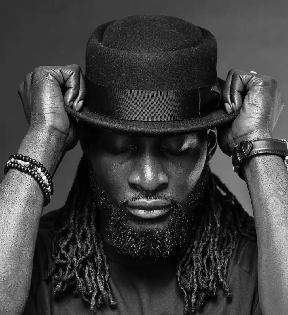 Black and white headshot of Kenrick wearing a black hat, with his eyes closed