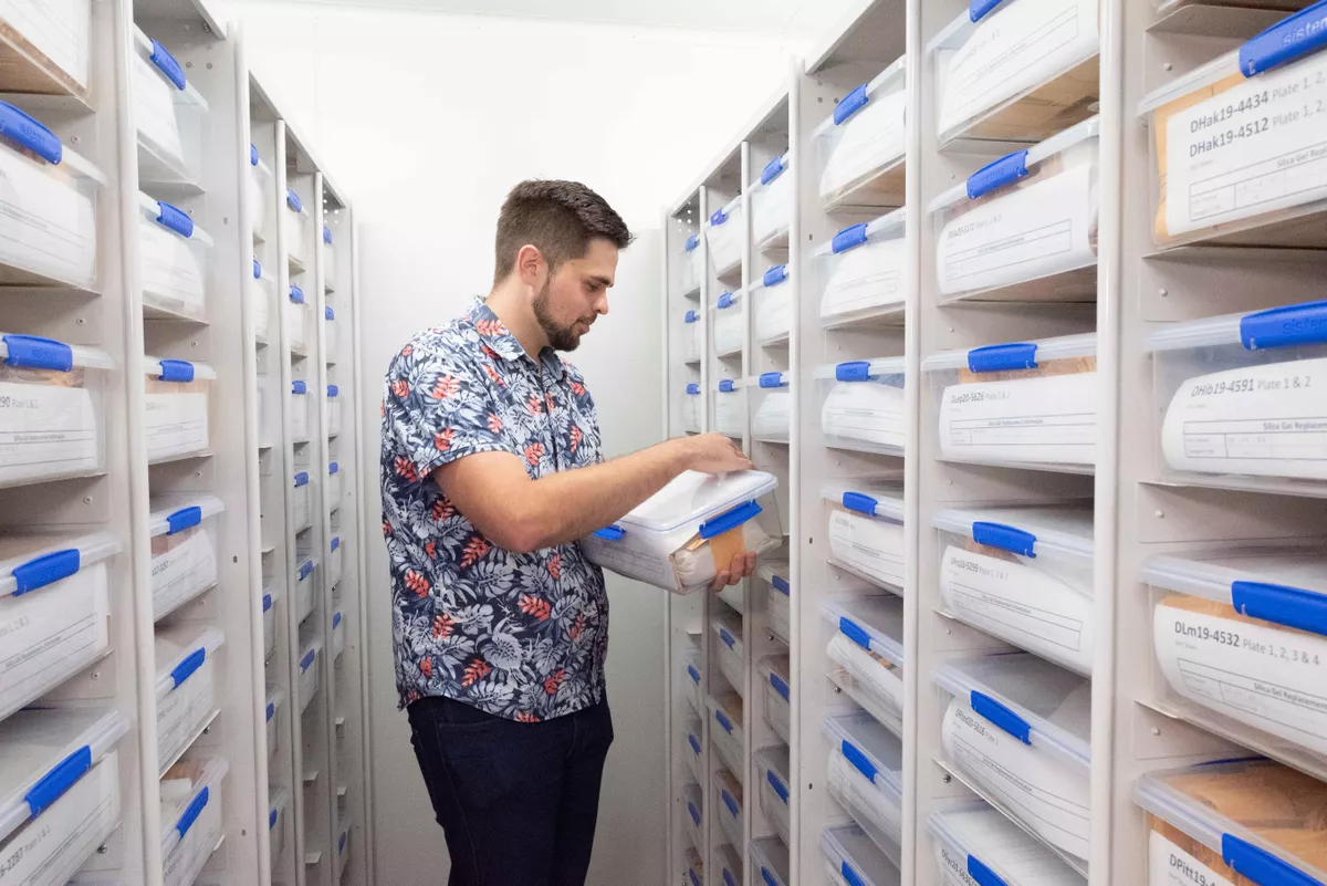 Someone examining a labeled plastic container in a storage room filled with shelves holding other containers
