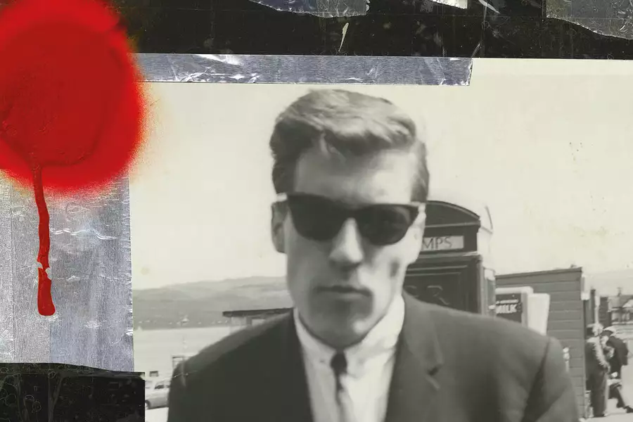 A black-and-white photo of a man wearing sunglasses and a suit, with a blurred background of a seaside scene. There is a bright red circle of paint on the photograph.
