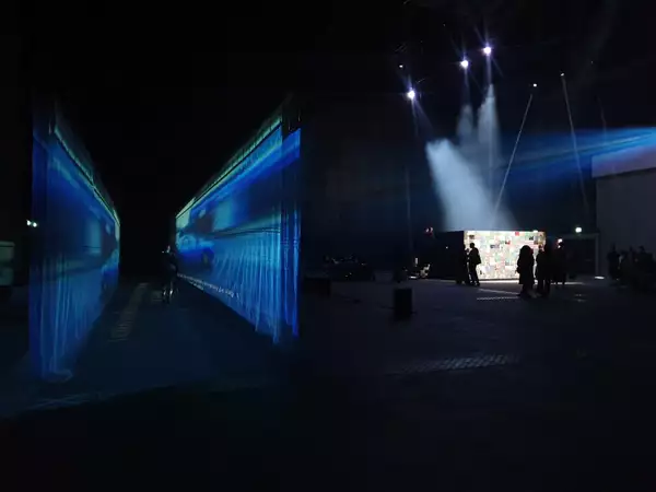 54: Manchester's installation in the warehouse – showing a fabric walkway with a film projected on to it and an enclosed, collaged box with performers inside
