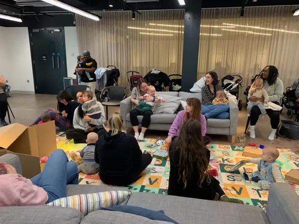 A group of first breath families sat on the sofas at Aviva Studios – plus babies playing on a mat decorated with the alphabet