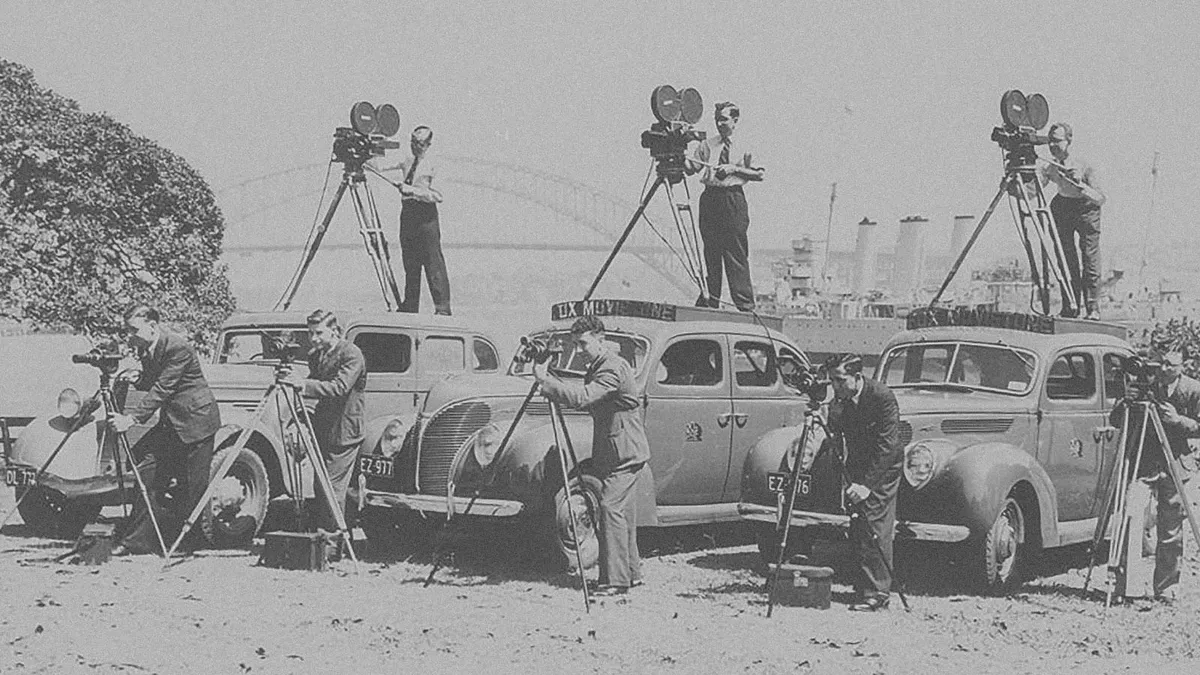 A group of men operating film and still cameras with the Sydney Harbour Bridge in the background.