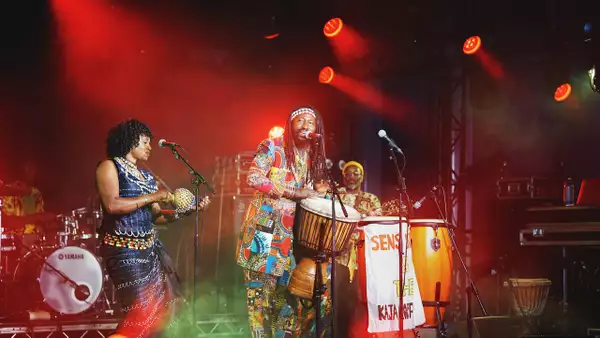 Two members of Sens Sagna & the Kajamor Family performing on the stage at Festival Square. The lighting is red.