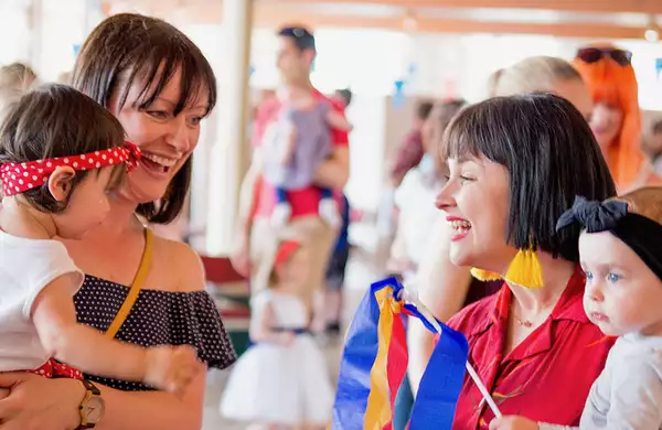Two parents holding their toddlers and smiling. The toddlers are wearing headbands.
