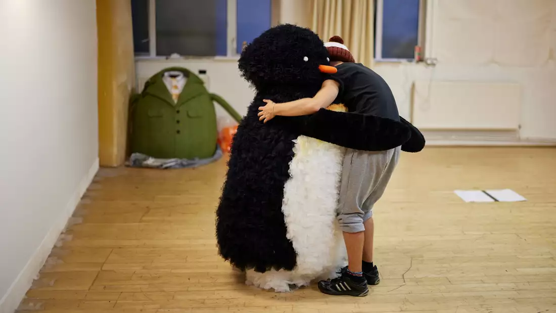 A puppet penguin and actor share a hug in Lost and Found rehearsals