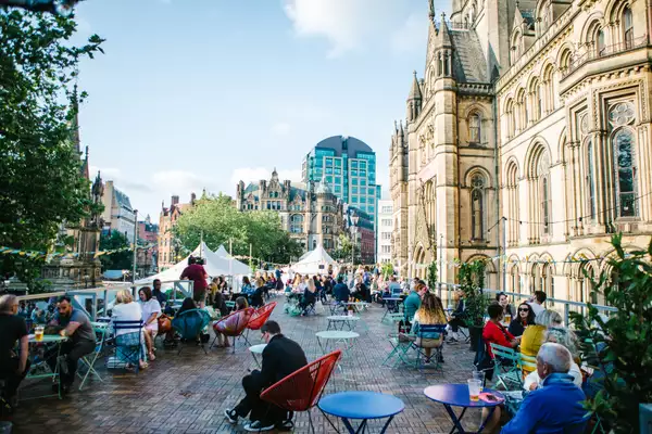 People sitting outside in the sunshine at tables in MIF's pop-up Festival Square in Manchester