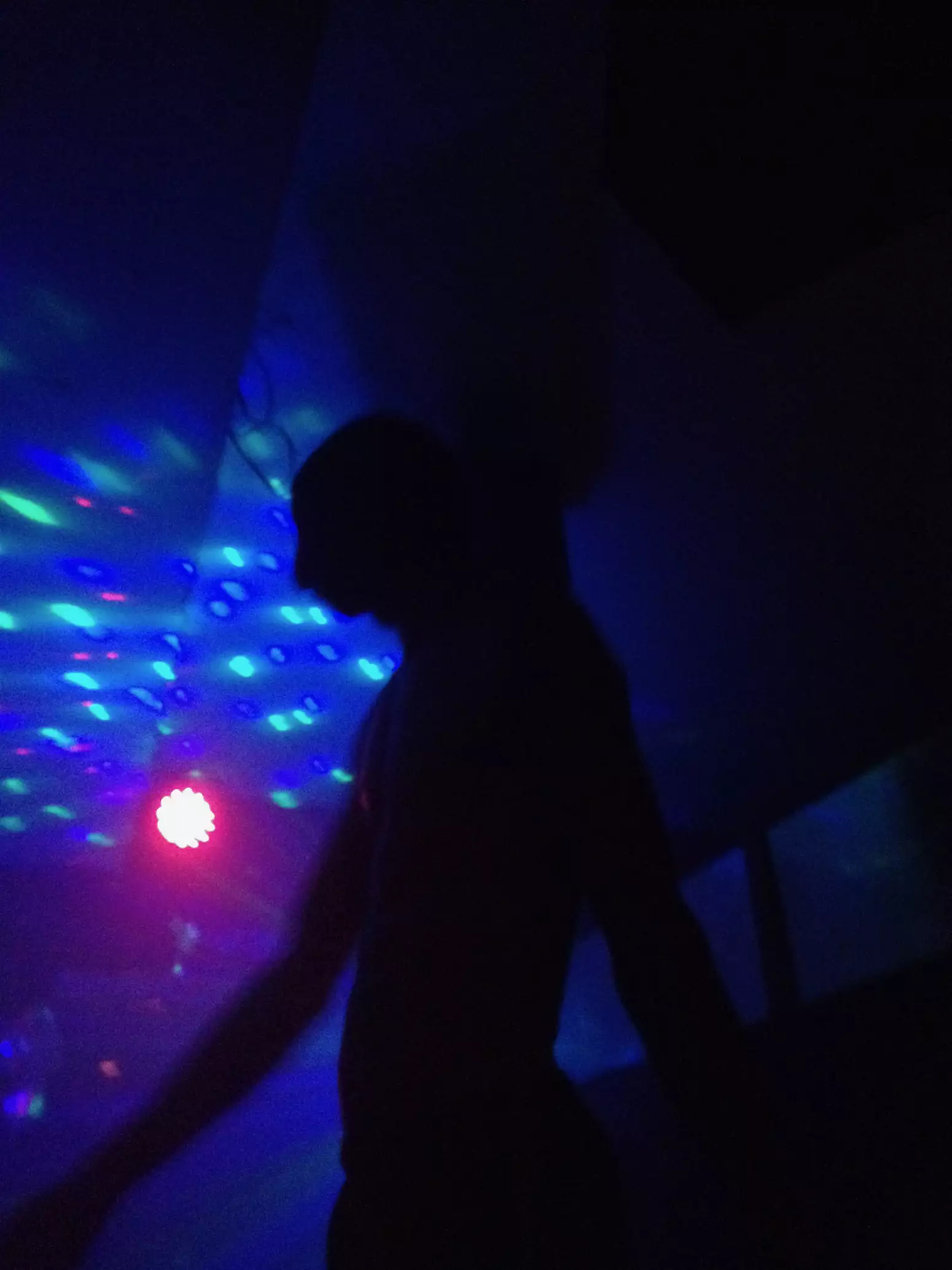 A person on a dancefloor with a multicoloured spotlight behind them