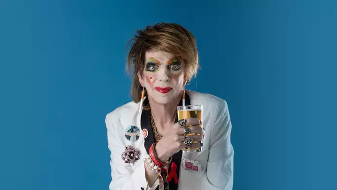David Hoyle holding a pint glass on a blue background