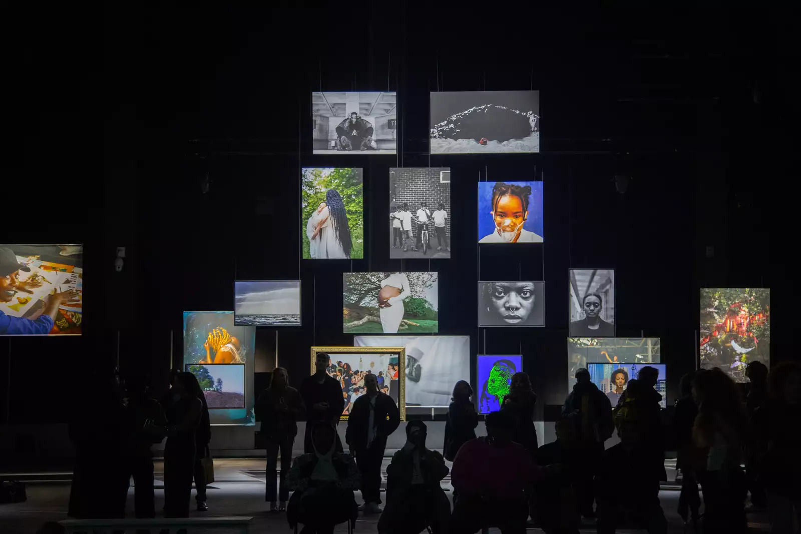 A group of people stood in the Reframe exhibition looking at the photographs, which are hanging from the ceiling of the Warehouse