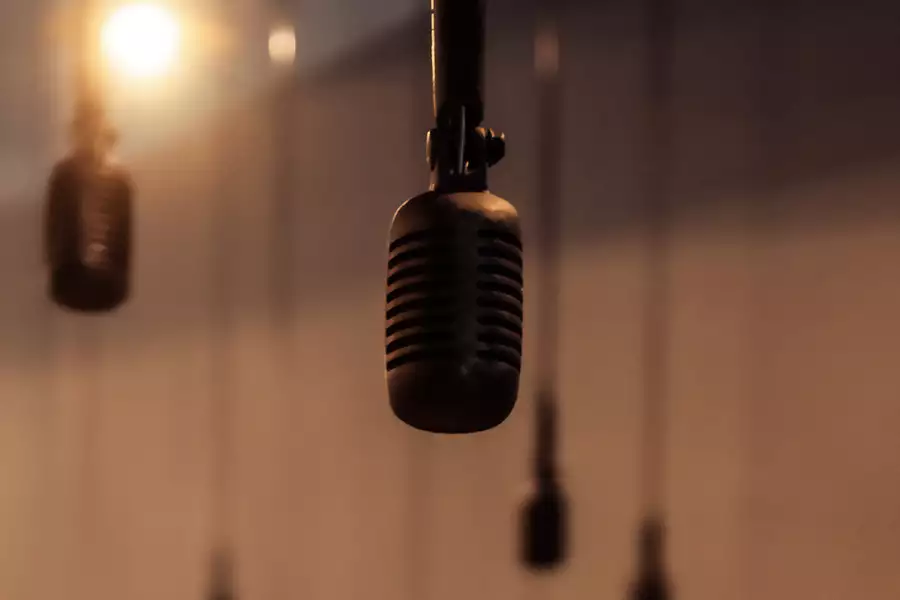 A close-up of a microphone hanging from above, with several similar microphones blurred in the background. The warm lighting and soft focus create an atmospheric feel.