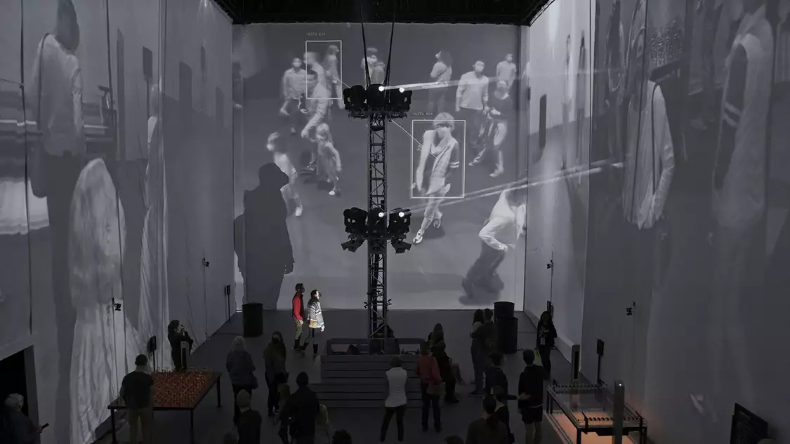 People viewing projections of faces on the walls of a gallery space