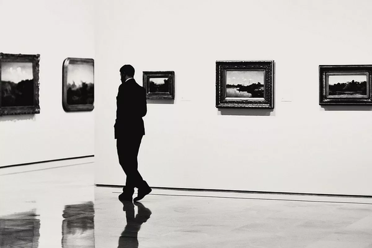 A man in a suit wanders through a gallery of framed landscape images