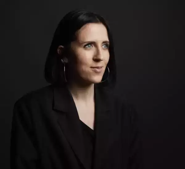 A portrait of artist and producer Nancy May Roberts wearing a dark jacket against a black background
