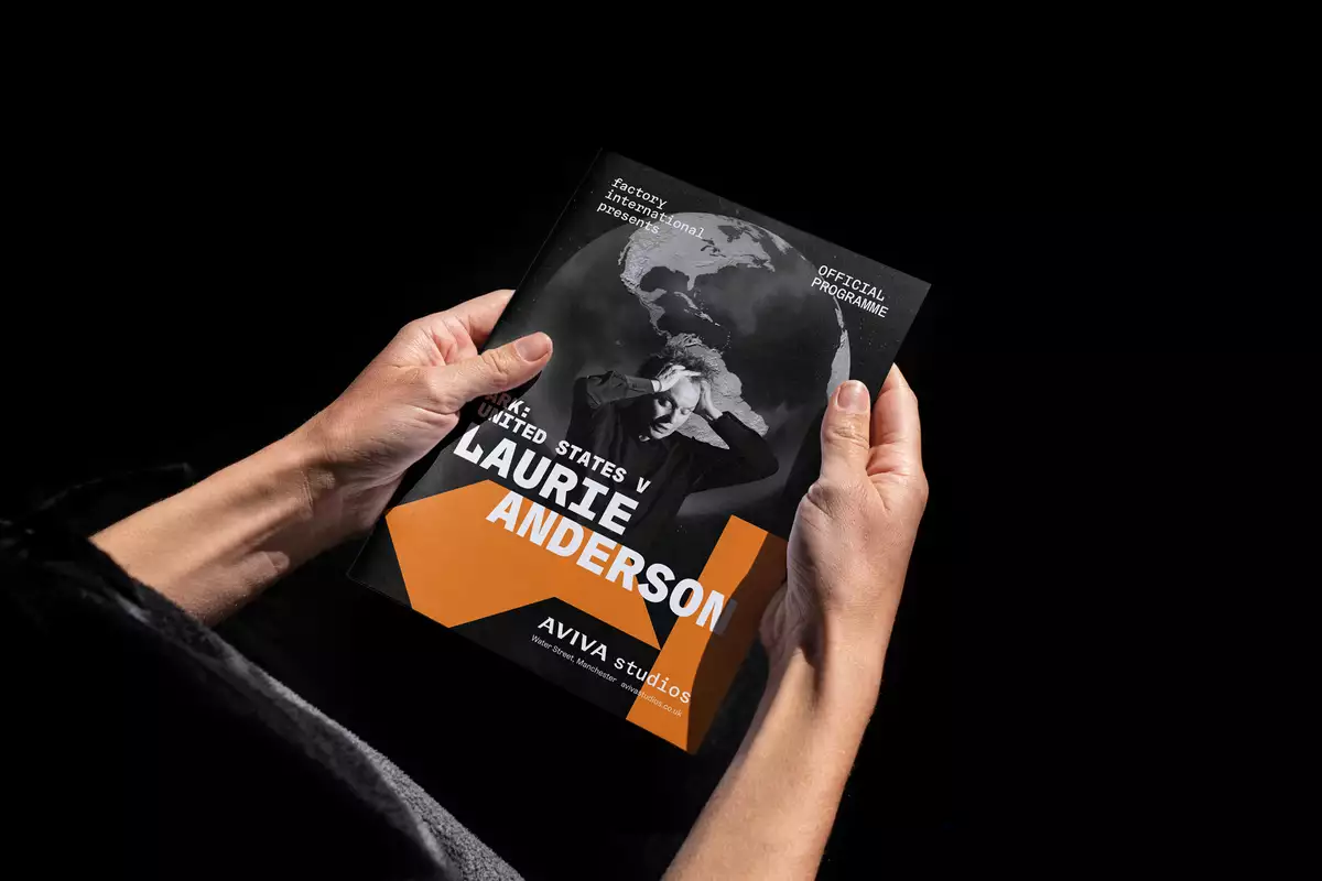 A pair of hands holding the programme for ARK United States V by Laurie Anderson