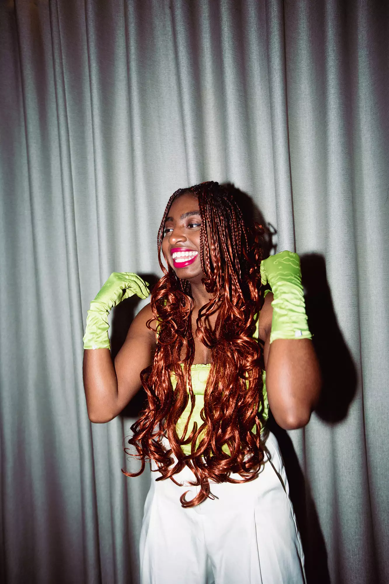 Factory+ Editor in Residence Kemi Alemoru wearing green gloves in front of a grey curtain