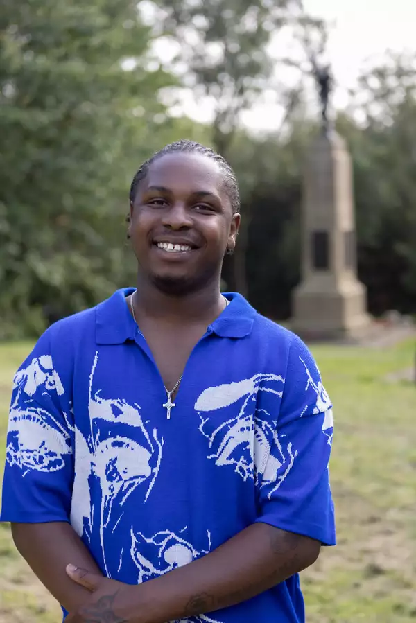 Headshot of Demereece Green wearing a bright blue and white shirt. They are stood outside in a park.