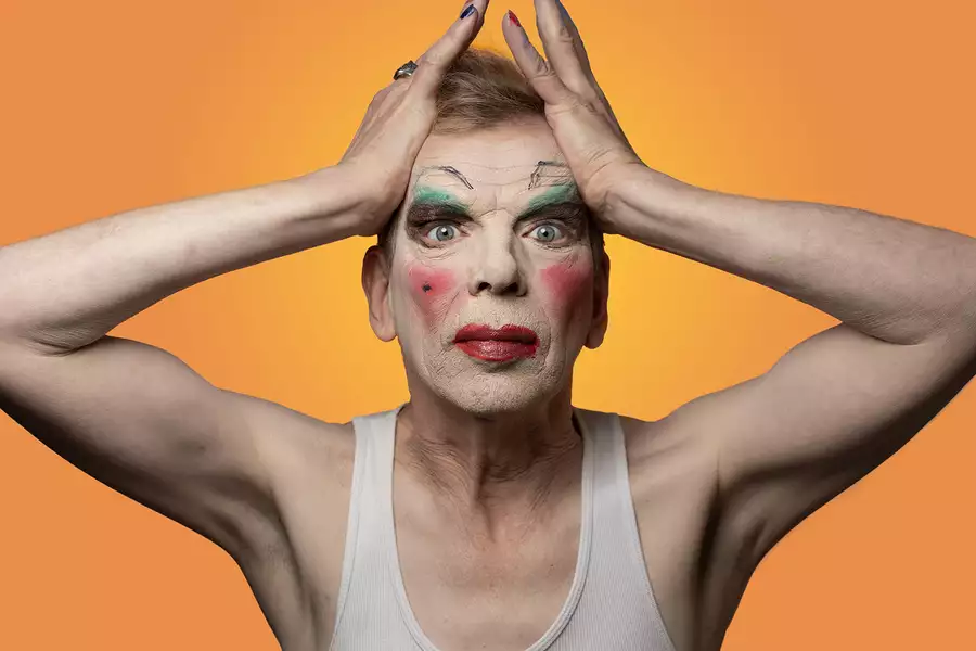 David Hoyle bold makeup and hands either side of his forehead against an orange background