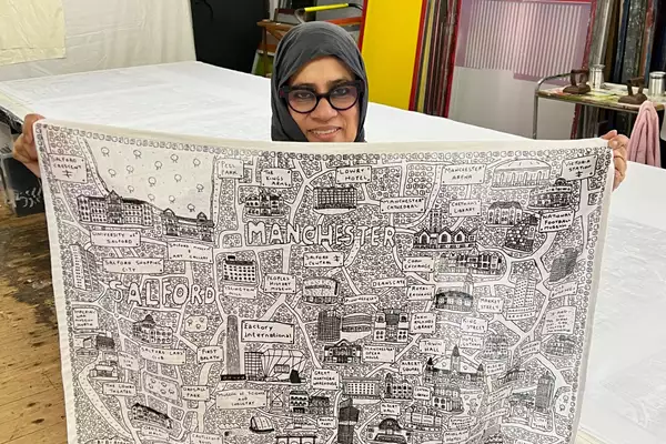 Taslima from CDM UK holds up a piece of fabric with a black and white print of Salford and Manchester