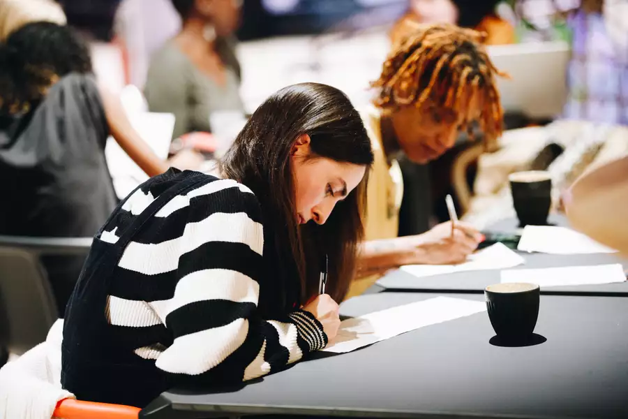 Two people writing with coffee mugs on the table