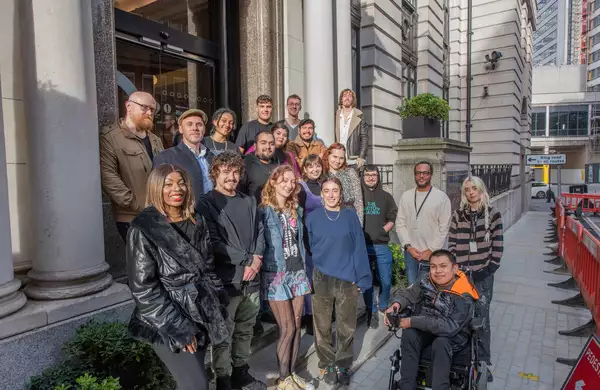 A group of people stand in front of an entrance to an office building, smiling and looking towards the camera.
