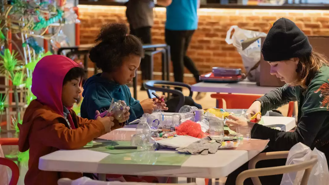 Two children and an adult sat around a table playing with crafts in the Social