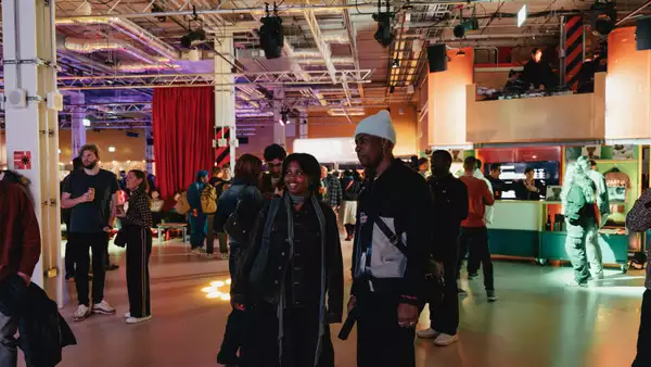 Two people stood smiling and chatting in the Social, which is busy with other people.