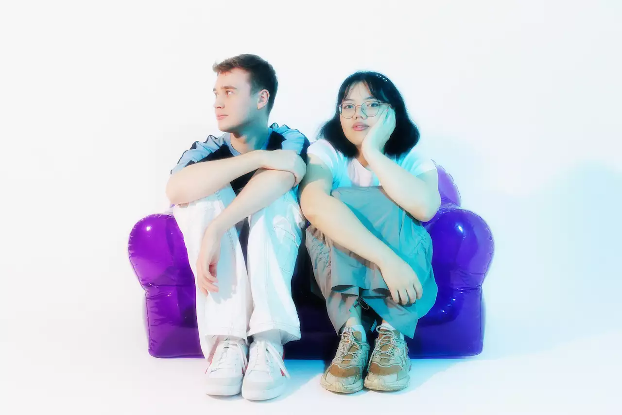 Two members of Beck Pocket sat on a bright purple inflatable chair. The background is white.