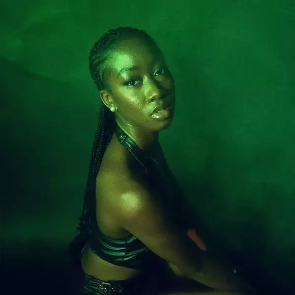 Headshot of DEELA in front of a dark green background