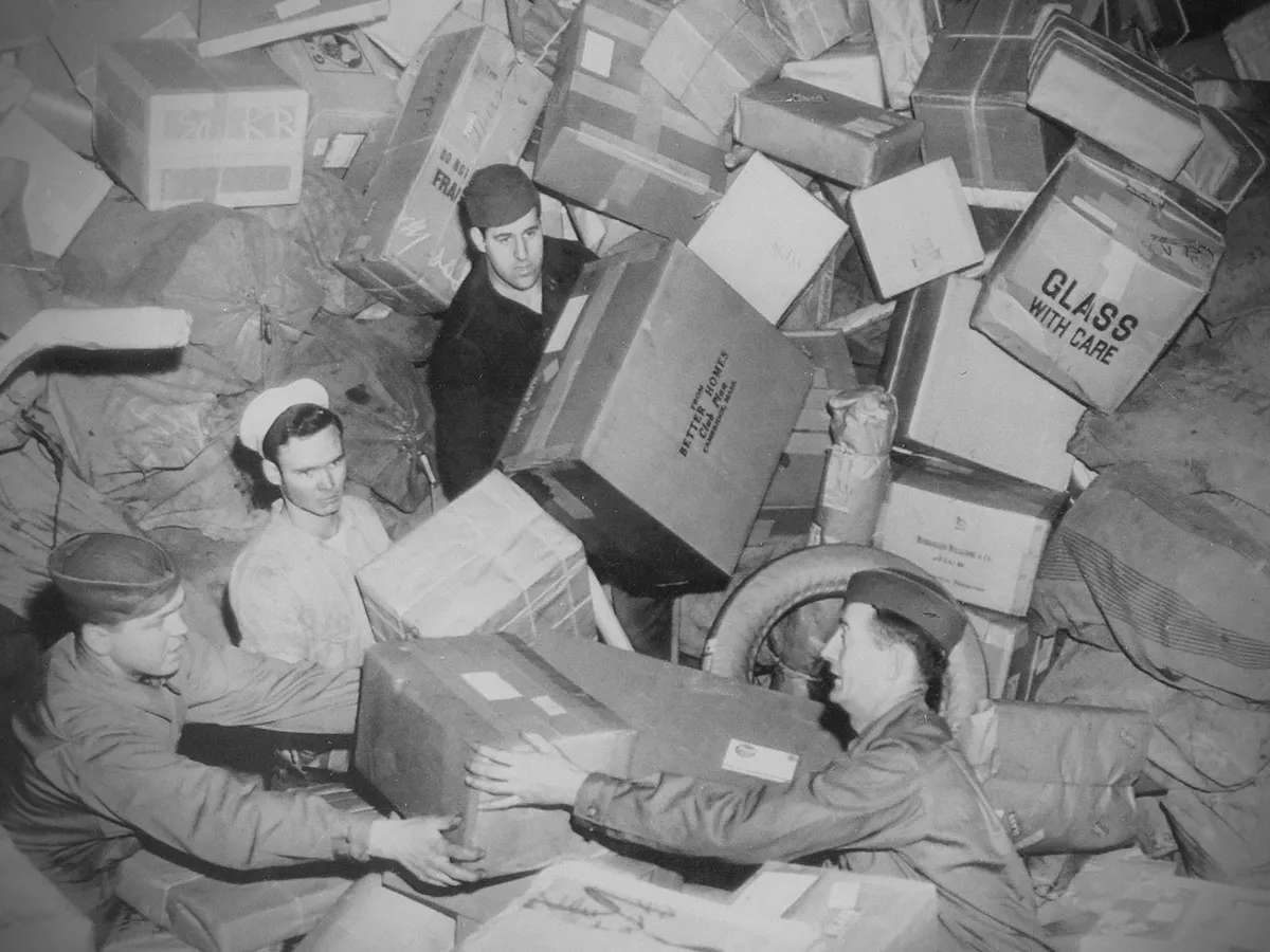 Three U.S. soldiers being almost buried by parcels at a mail depot during World War 2, circa 1944