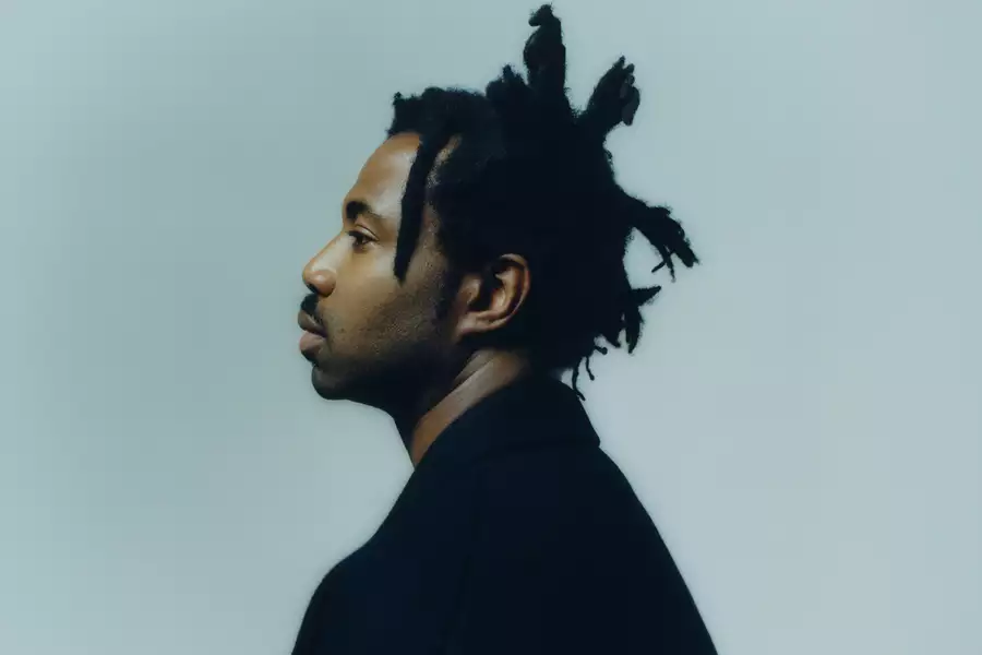 Side angle of Sampha on a light blue background