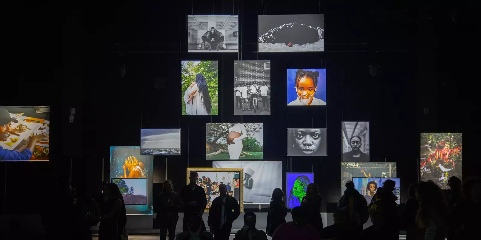 A group of people stood in the Reframe exhibition looking at the photographs, which are hanging from the ceiling of the Warehouse