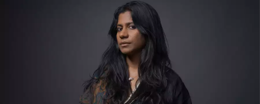 Headshot of ganavya wearing a black shirt and patterned brown scarf on a black background
