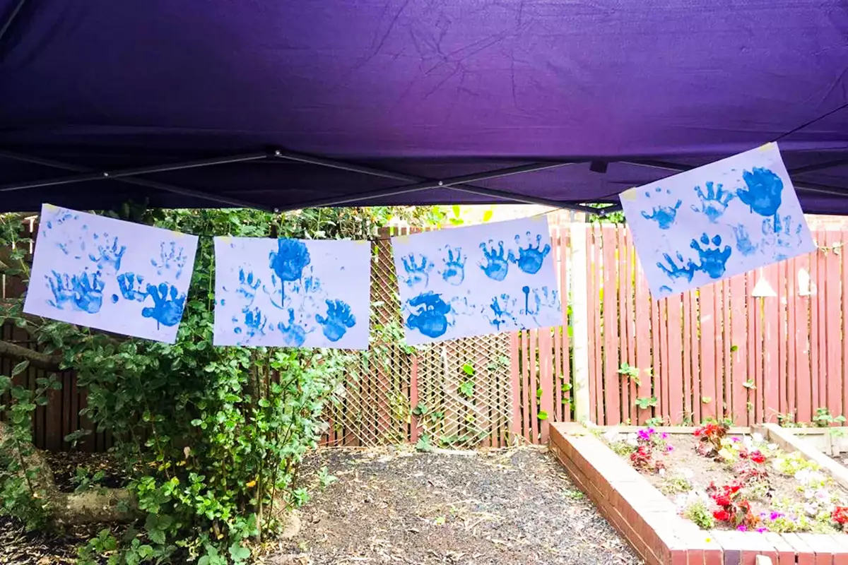Four white sheets of paper are hung on a washing line. On each sheet there are multiple hand prints made in blue paint.