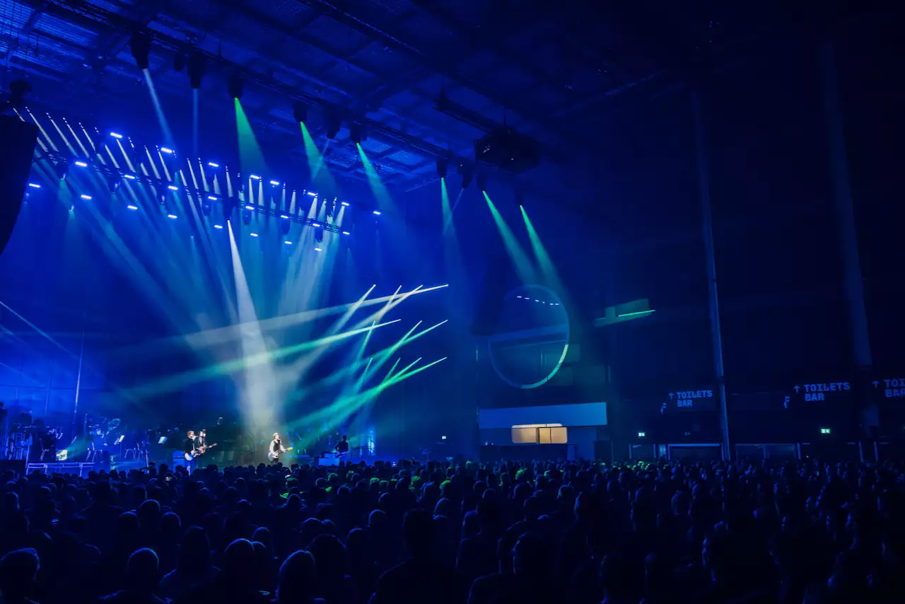 A large crowd watches Johnny Marr on stage in the Warehouse. The lighting is dark blue.