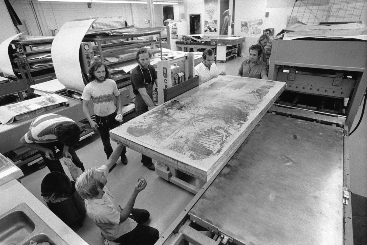Robert Rauschenberg observes Daniel Freeman, Andrew Vlady, Bob Petersen, Tim Ifsham, Charles Ritt and Ron McPherson move laminated lithography stone for 'Waves' print from 'Stoned moon' lithographic series onto lithography press bed, in workshop, Gemini G.E.L., Los Angeles, 1969