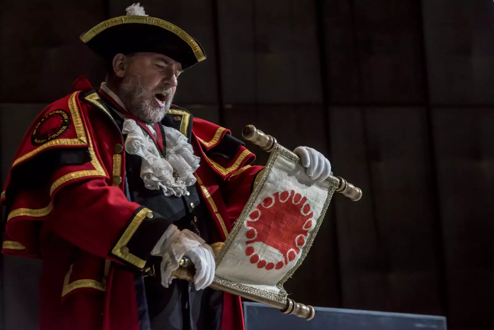 A town crier reading from a scroll during the Summer 2024 Artist Takeover