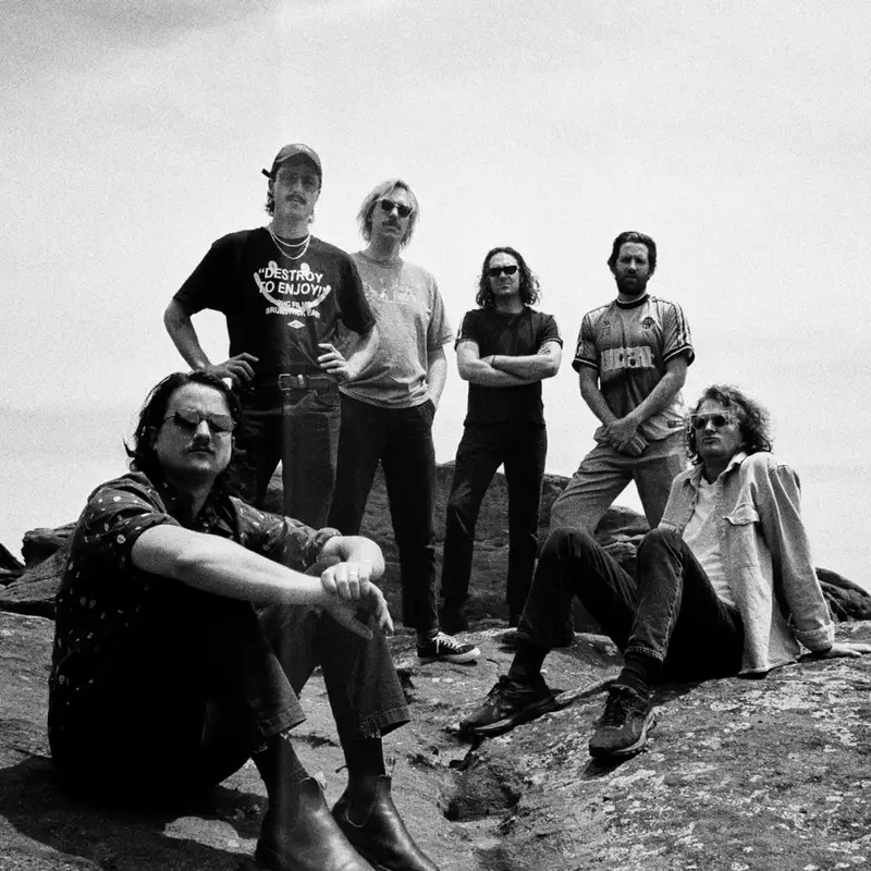 A black and white photo of six members of King Gizzard & The Lizard Wizard posing on a rocky landscape.