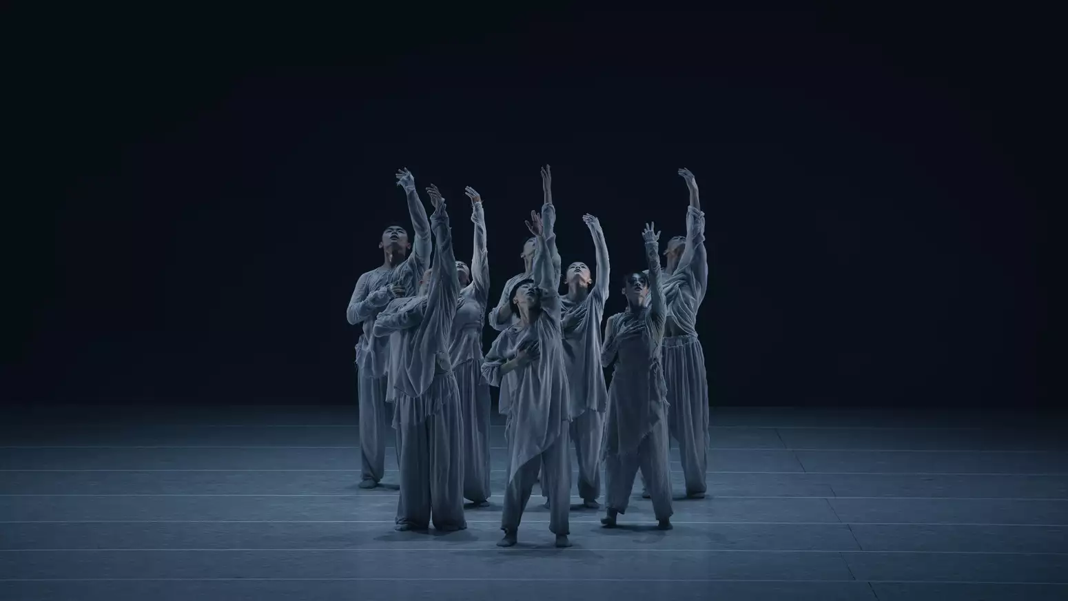 Eight dancers performing on a stage – their hands pointing in the air and looking upwards