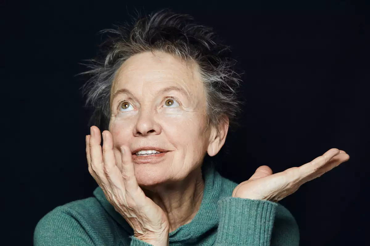 A photograph of artist Laurie Anderson seated in a green jumper