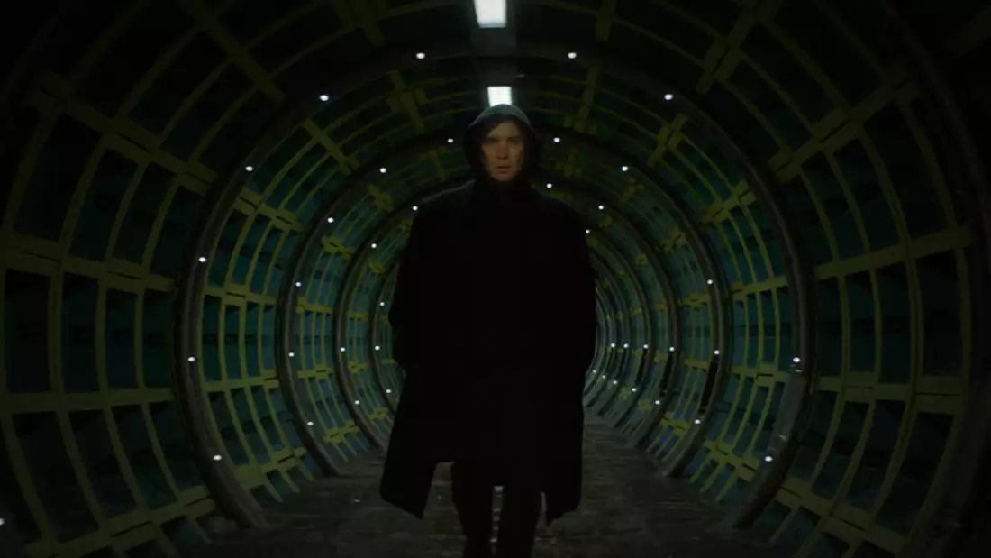 A still from All Of This Unreal Time, with Cillian Murphy walking towards the camera in a long, straight tunnel with green metal walls.