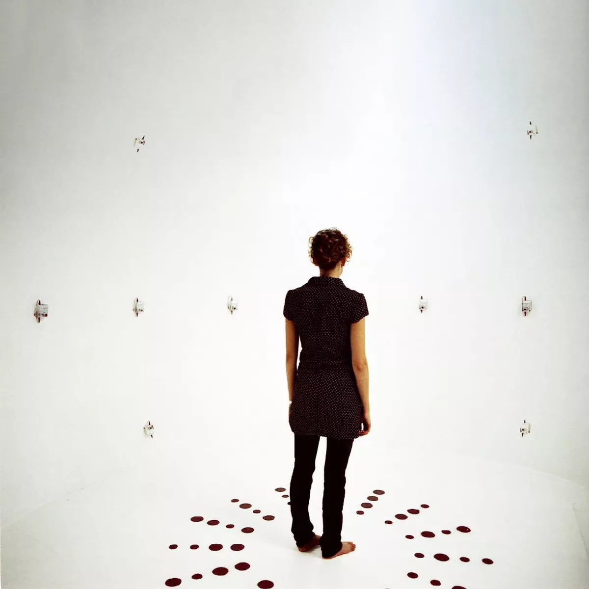 Someone standing in the middle of an empty room with blank white walls and surrounded by tiny cameras.