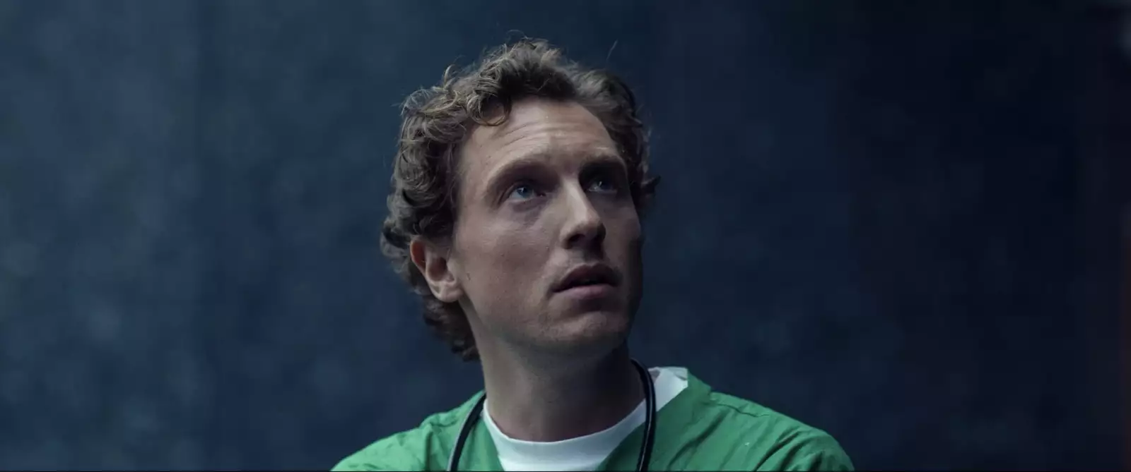 Still from In Camera. Rory Fleck Byrne wearing green scrubs and looking upwards.