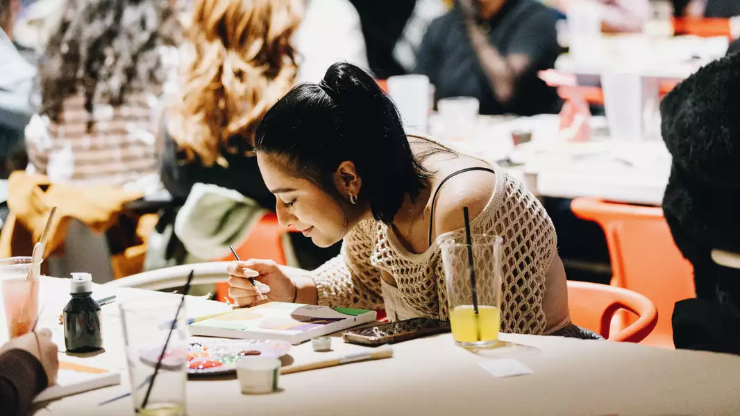 A person painting a canvas and smiling at a Sip and Paint class